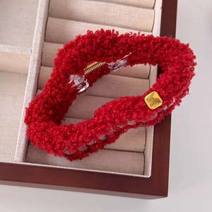 Détail d'une pince à cheveux en peluche rouge avec étiquette dorée sur tissu beige