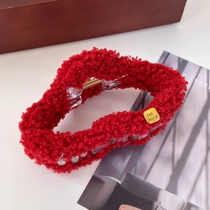Détail d'une pince à cheveux en peluche rouge avec texture polaire et logo doré