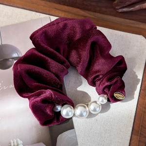 Detailed view of burgundy velvet scrunchie with elegant pearls and golden logo tag