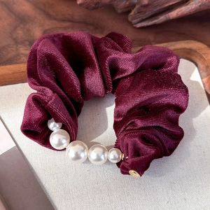 Detailed view of burgundy velvet scrunchie with elegant faux pearl accents on fabric