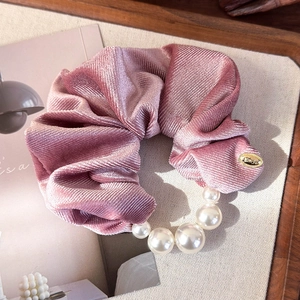 Detail of pink velvet scrunchie with gradient pearls and a gold logo charm for women