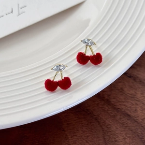 Detail of red velvet cherry earrings with crystal leaf on a white ceramic plate