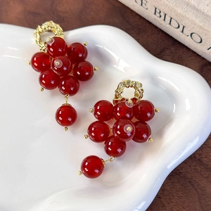 Vintage gold hoop earrings with dark red grape cluster beads on a ceramic plate