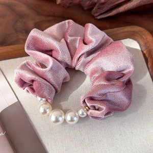 Detail of pink velvet scrunchie with pearls on a natural wood and beige fabric tray