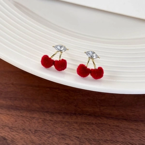 Detailed macro view of cherry stud earrings with red velvet finish and gold leaf accents
