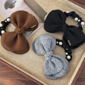 Three wool bow hair scrunchies with faux pearls and metal tags in a woven tray