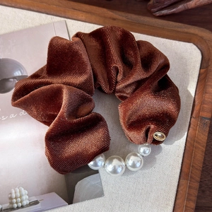 Detail of caramel velvet scrunchie featuring elegant pearls and gold metallic logo tag