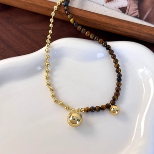 Detail of tiger eye stone and gold bead necklace with two spherical pendants on a tray