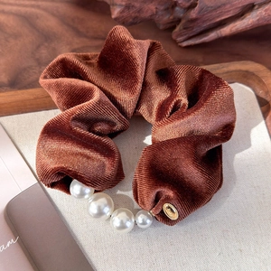Detail of burgundy velvet scrunchie with faux pearls and golden tag on a texture board