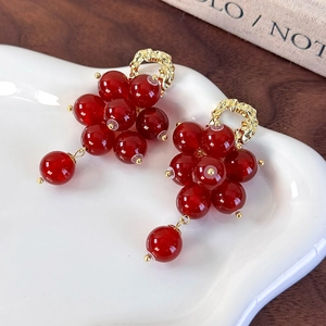 Close-up of vintage red grape bead tassel earrings on a white ceramic tray