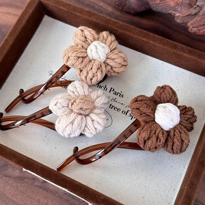 Détail de trois barrettes fleurs en tricot beige et marron sur présentoir velours