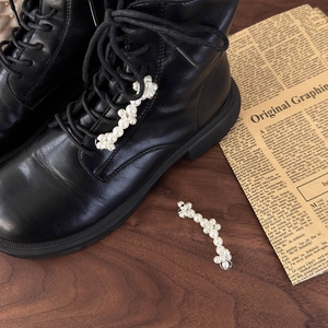 Detailed close-up of pearl flower shoe charms on black leather boots with metal clips