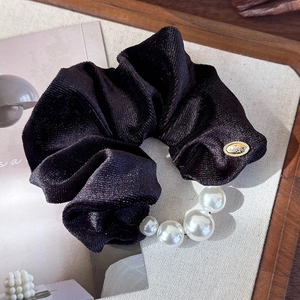 Detail view of black velvet scrunchie featuring elegant white pearls and a gold metal tag