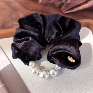 Detail of elegant black velvet hair scrunchie with white pearls and gold metal accent