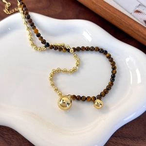 Detail of tiger eye beads and gold metallic spheres on a two-tone necklace over ceramic