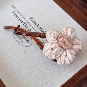 Détail d'une pince à cheveux banane en acrylique marron avec fleur en laine crème