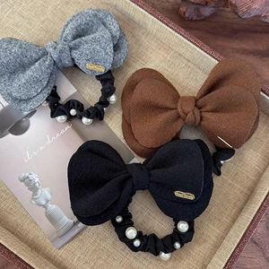 Detail of wool bow scrunchies in grey, brown, and black with pearls in a woven tray
