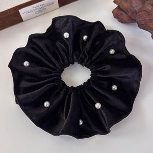 Detail of a black velvet scrunchie with textured fabric and white pearl embellishments