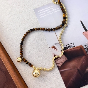 Detail of tiger eye stone beads and polished gold sphere pendants on a linen background
