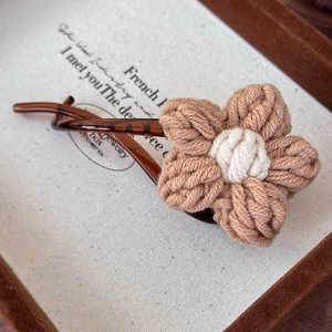 Détail d'une pince à cheveux fleur en laine marron tricotée main sur fond vintage