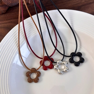 Detalle de cuatro collares de flores en marrón, rojo, plateado y negro sobre plato de cerámica
