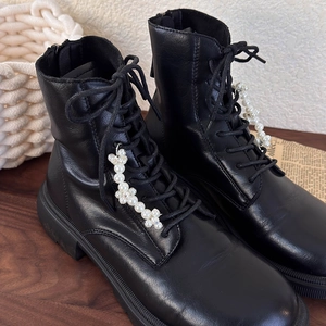Black leather boots with white pearl flower charms on a rustic wooden table