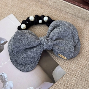 Detail of grey wool bow hair scrunchie with faux pearls and gold logo on woven surface
