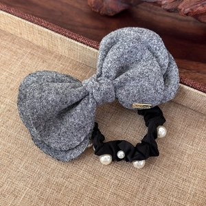 Detail of wool bow hair tie with white pearls and gold handmade tag on linen base