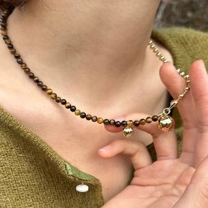 Tiger eye and gold bead asymmetrical necklace with spherical pendants on model neck