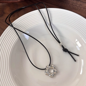 Detalle de un colgante de flor plateada en un cordón negro ajustable sobre un plato de cerámica
