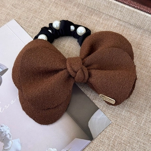 Detail of brown wool bow hair scrunchie with white pearl accents and handmade metal tag