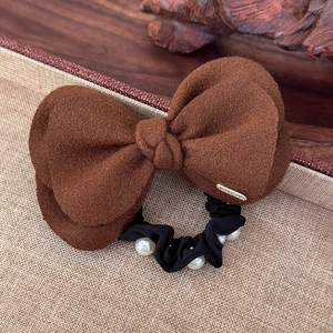 Detail of wool bow hair tie with cream pearls and gold tag on brown textured fabric