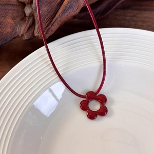 Detalle del colgante de flor de cerámica rojo oscuro en cordón trenzado