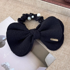 Close-up of black wool bow hair tie with white pearls and gold Hand Made metal tag