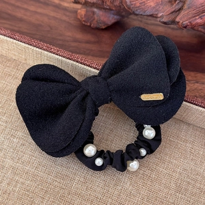 Detail of black wool bow hair tie with white pearls and gold handmade tag on beige base