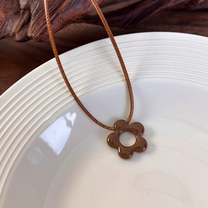Primer plano de un collar con colgante de flor marrón brillante en una bandeja de cerámica