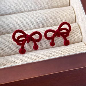 Detail view of retro red velvet bow earrings displayed in a beige textured jewelry box
