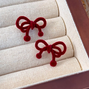 Close-up of vintage red velvet bow earrings with small sphere drops on beige texture
