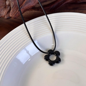 Detalle macro del colgante de flor negra minimalista con cordón sobre un plato