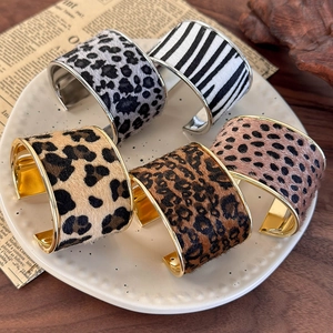 Detailed view of animal print suede cuffs with gold and silver metal lining in a tray