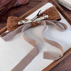 Close-up of vintage brown embossed bow hair clip with velvet ribbons on a wood tray