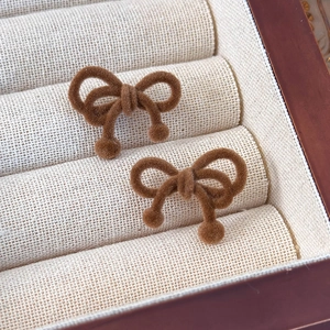 Close-up of brown velvet bow stud earrings with small ball charms in a jewelry box