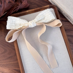 Detail of elegant white lace bow hair clip with long beige ribbons on a wooden tray