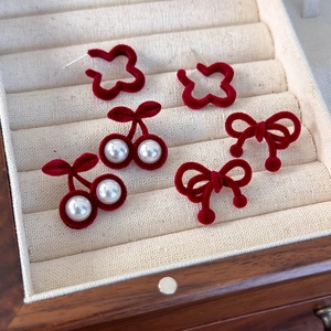 Détail de boucles d'oreilles cerise et nœud en velours rouge dans un écrin en bois