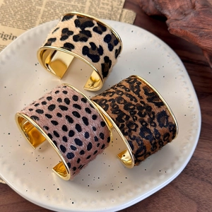 Detail of three leopard print wide open bangles with gold metal edges on a tray