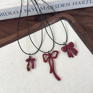 Close-up of three dark red bow pendants on black cords over a wooden display tray