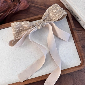 Detail of elegant beige bow hair clip with lace texture and long silky ribbons