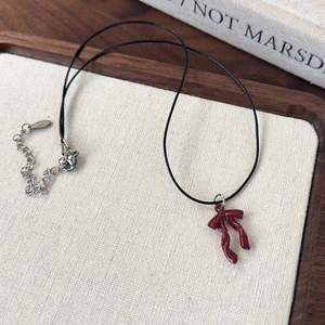 Close-up of red bow pendant on black wax cord with silver extender chain detail