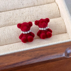 Gros plan de boucles d'oreilles ours rouge floqué avec collier de perles et texture velours