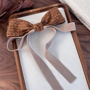 Detail of vintage brown jacquard bow hair clip with long velvet streamers on linen board